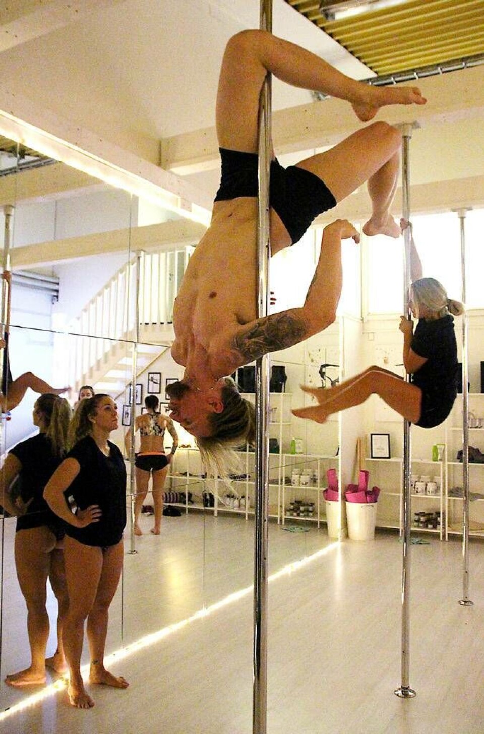 Ägaren Natalie Tähtinen kollar in adepten Christoffer Gråds akrobatiska övningar på stången. ”Det är rätt så tuff, det är mycket vad man gör av det själv”, säger han om poledance. Foto: Jonas Bergkvist