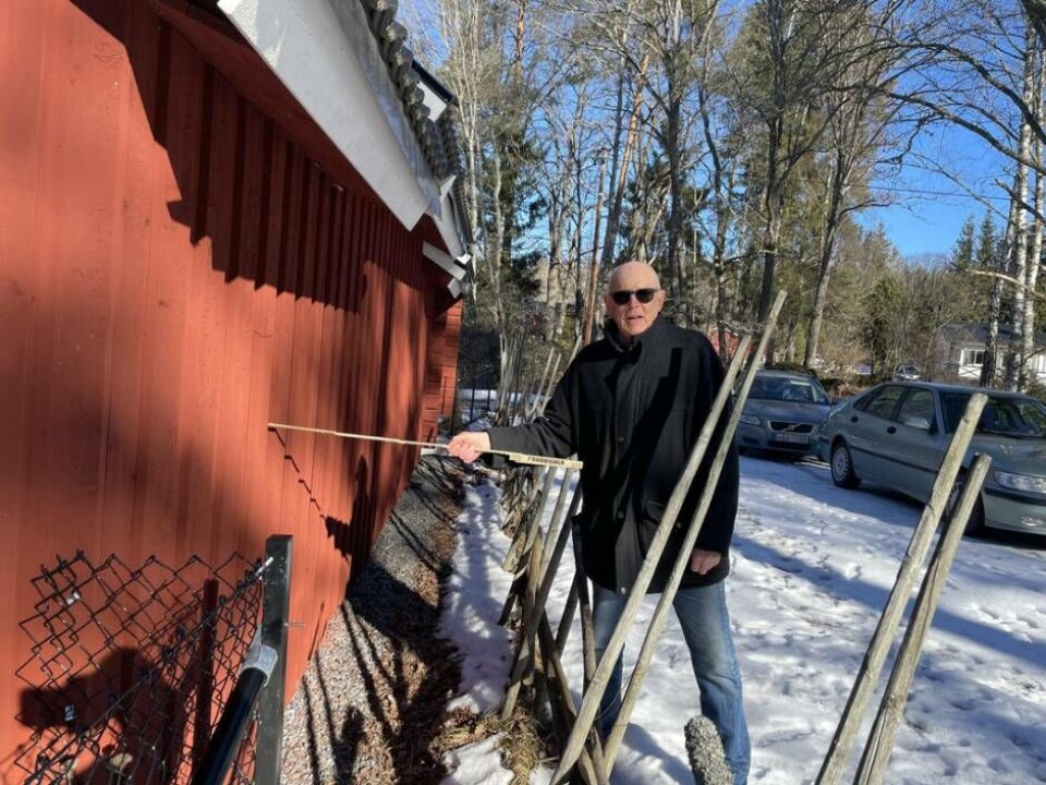 Måttstrid. Curt Holmbäck visar med tumstocken hur nära tomtgränsen grannens uthus är byggt. Med tummen markerar Curt var tomtgränsen går. Foto: Jonas Edberg
