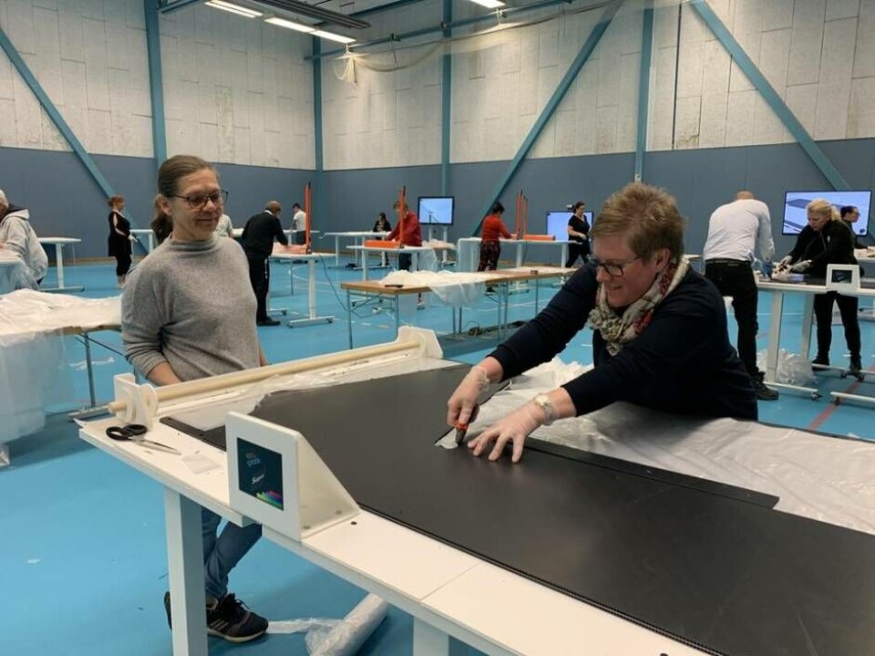 Maria Hennig, ekonomichef på Regional utvecklingsförvaltning, och Josefin Eller från Folktandvården på Vallby hjälps åt med att tillverka förkläden i den nyöppnade tillfälliga fabriken i Västerås Arena. Foto: Jonas Edberg