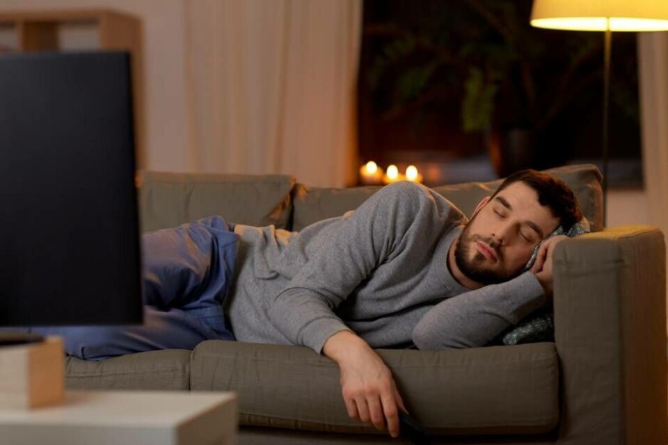 leisure and people concept - man sleeping on sofa with tv on at home at night Foto: lev dolgachov